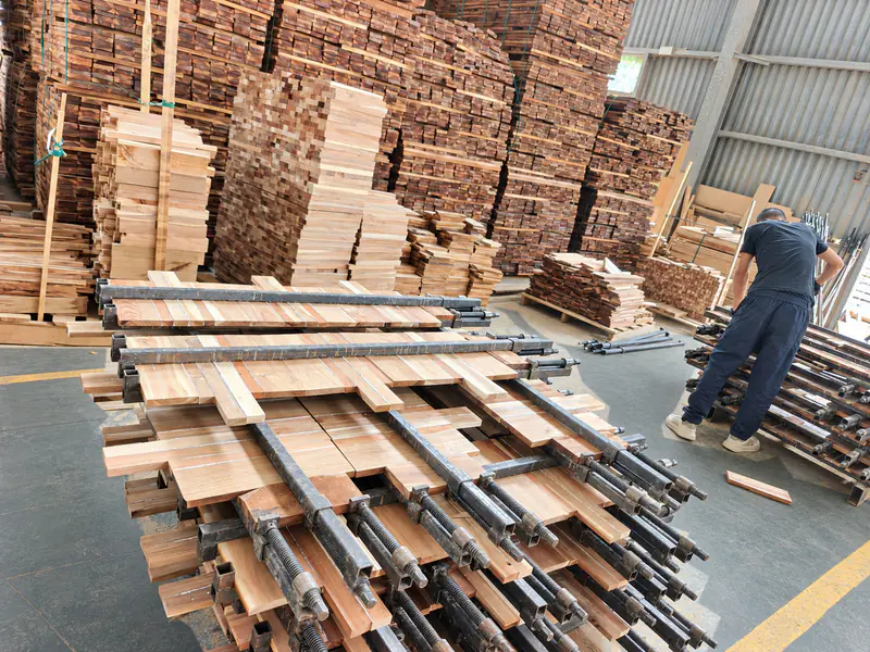 Acacia wood sections positioned in panel clamps beside stacked timber