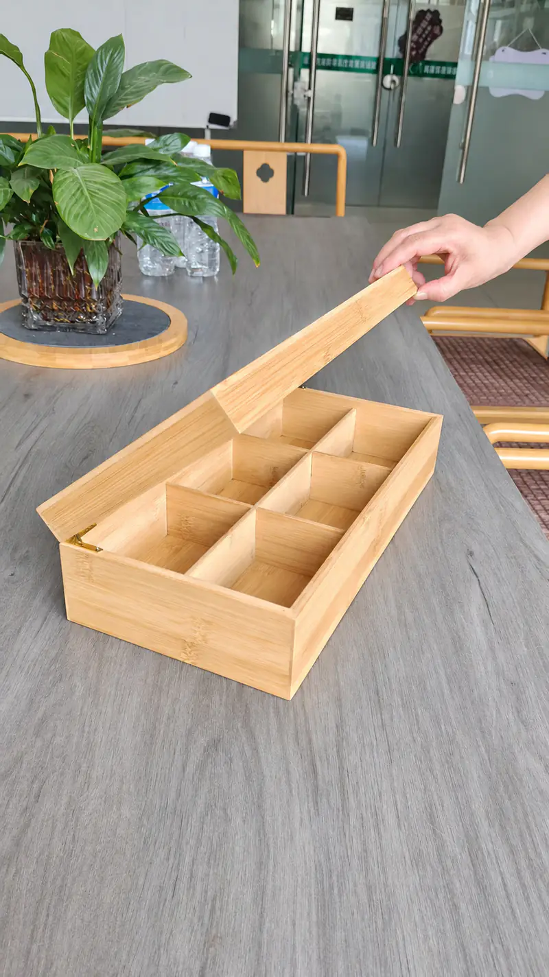 A hand opening the lid of a divided bamboo box sample