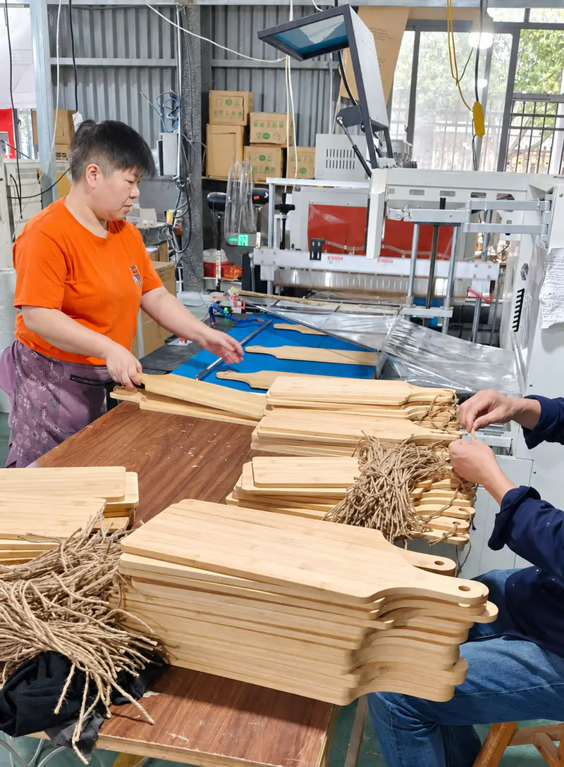 Workers attaching hanging cords to cutting boards on an assembly table